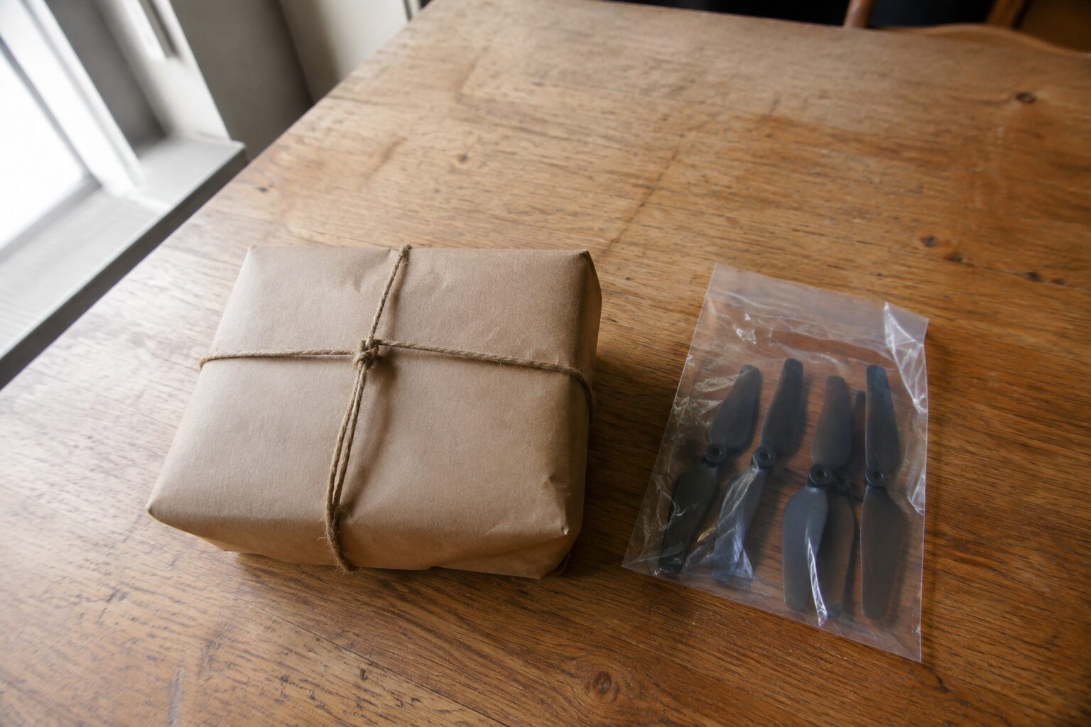 Een klein bruin pakje met een touwtje eromheen naast een setje propellers in verpakking zonder opdruk