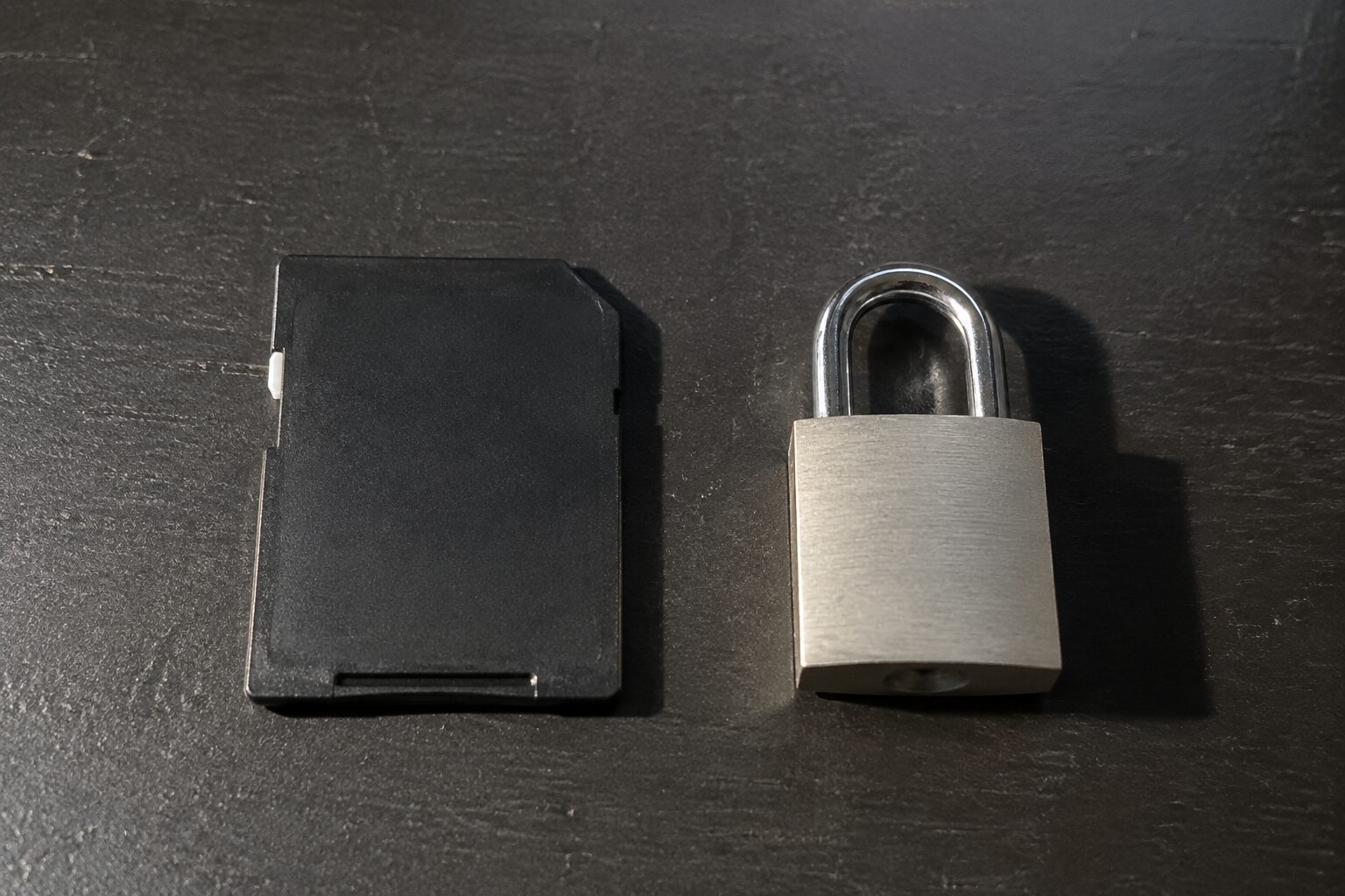 Een SD-kaart en een klein metalen hangslotje naast elkaar op een donker bureau